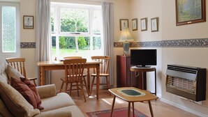 A living room with a sofa, chairs, a TV, a fireplace, and a dining table. - 2 bedroom accommodation in Wells-next-the-Sea (Wells-next-the-Sea)