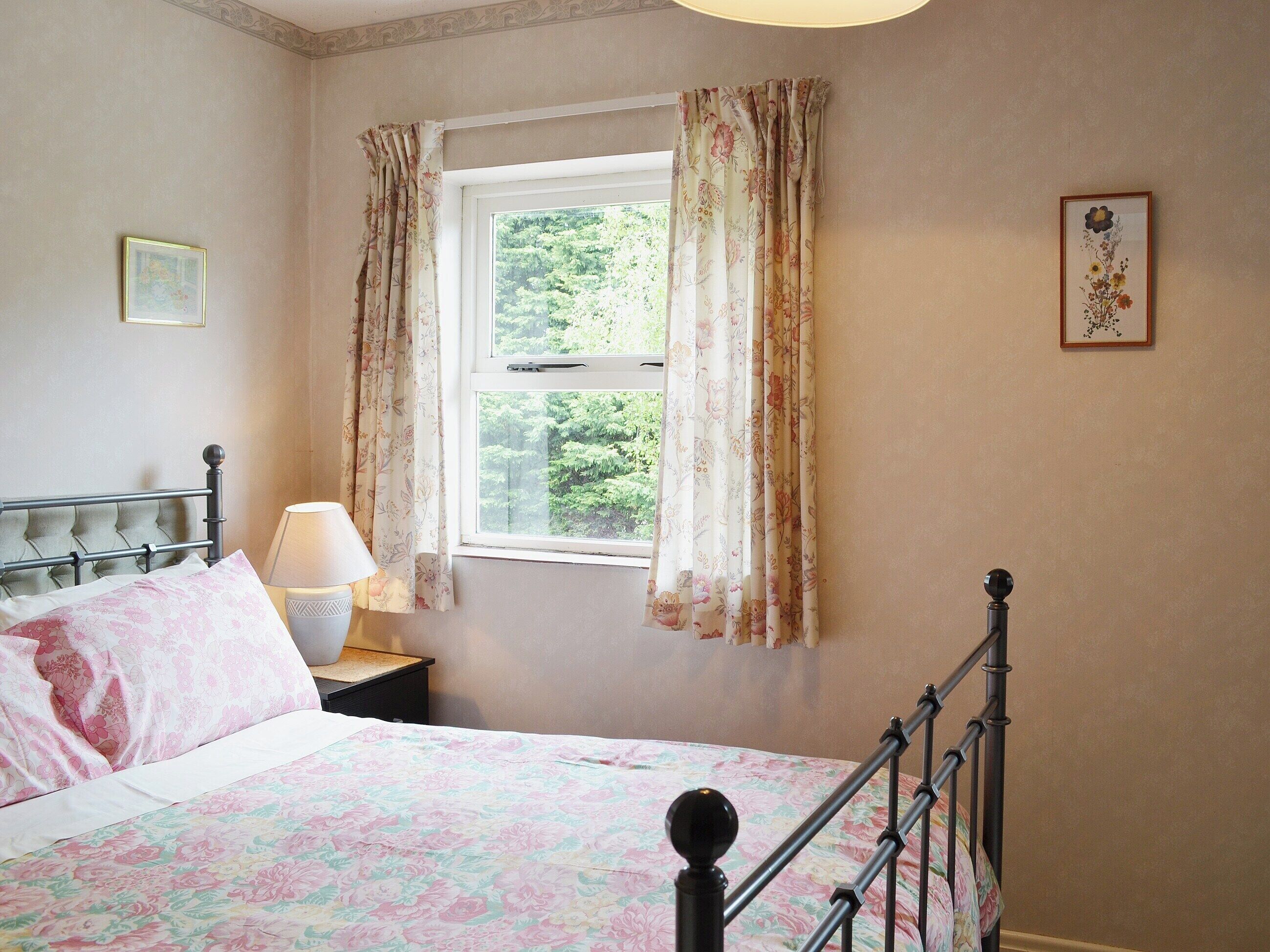 A bedroom with a bed, a nightstand, a lamp, a window with curtains, and a framed picture on the wall.