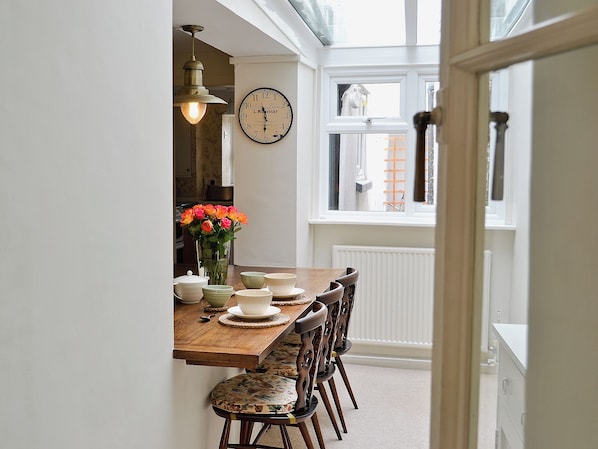 A dining area with a wooden table, chairs, a vase of flowers, and a wall clock.