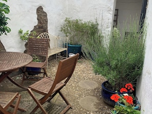 A patio with a round table and wooden chairs, surrounded by potted plants and a stone wall.