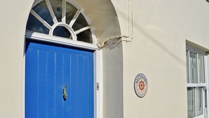 En blå dør med et skibsrat-emblem, et vindue og en hvid væg.