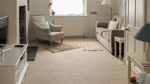 En stue med sofa, lænestol, fjernsyn, lampe og et vindue med gardiner.