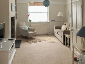 Een woonkamer met een bank, fauteuil, televisie, lamp en een raam met gordijnen.
