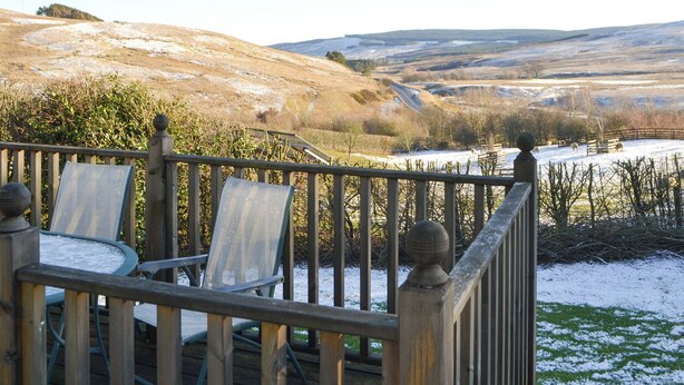 Terraza con sillas y una mesa, con vistas a un paisaje nevado con colinas y un área cercada con animales.