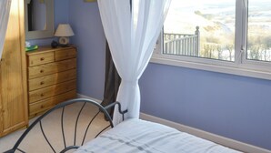 Un dormitorio con cama, cómoda de madera, espejo y ventana con vista al campo.