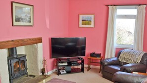 Una sala de estar con chimenea, televisor, sofá de cuero y una ventana con cortinas.