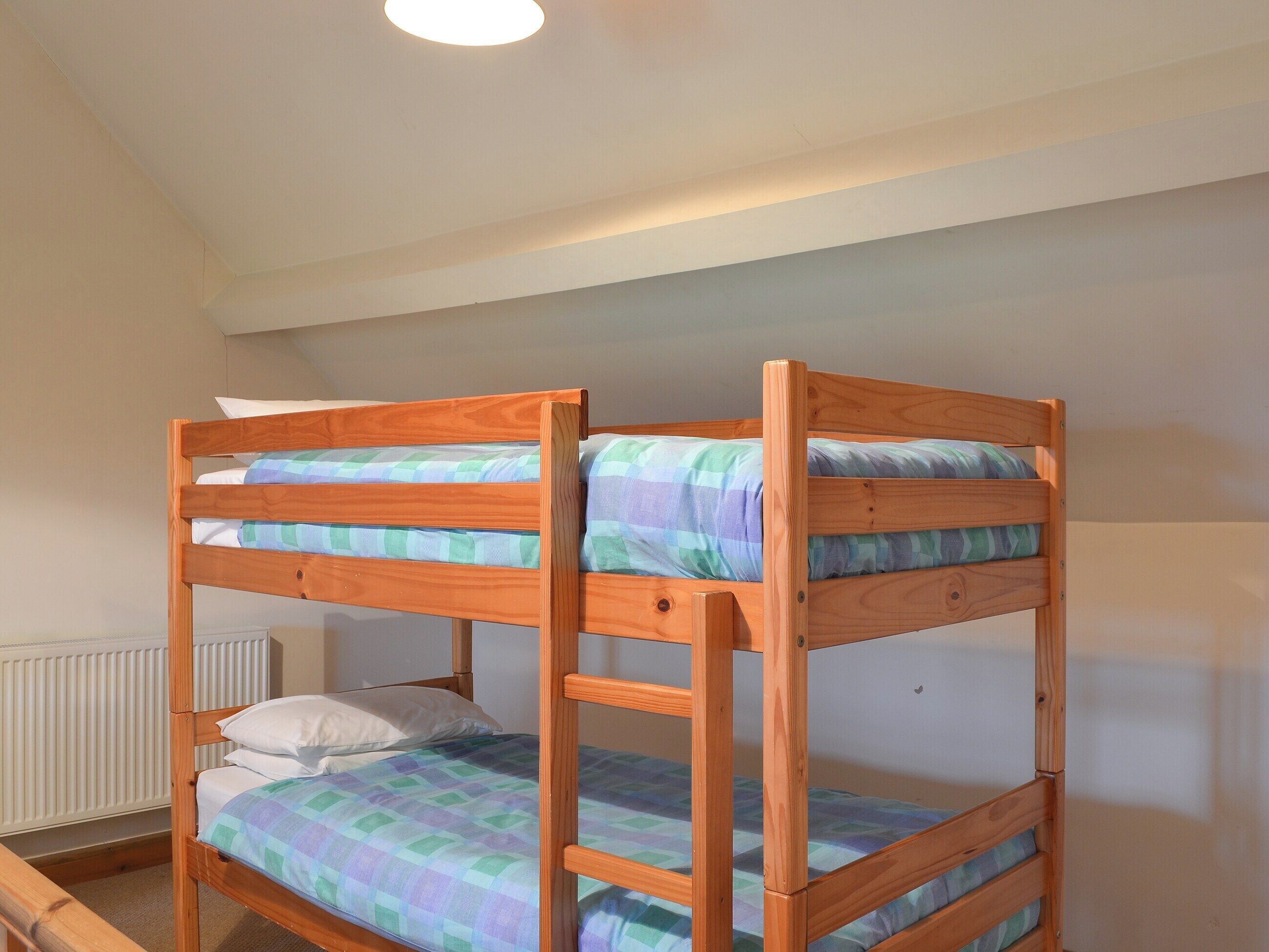 A bunk bed with a checkered bedspread in a room with a radiator and a plain wall.
