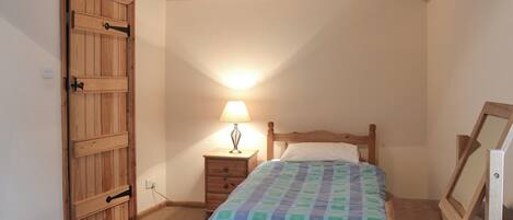 Ein Schlafzimmer mit einem hölzernen Bett, einem Nachttisch mit Lampe, einem Holzschrank und einem an der Wand leanenden gerahmten Bild.