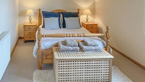 Un lit bien fait, avec une tête de lit en bois, deux tables de chevet avec des lampes, un petit tabouret en bois et un tapis blanc.