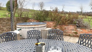 Une terrasse extérieure avec une table ronde en métal, quatre chaises, un jacuzzi et un mur en briques.