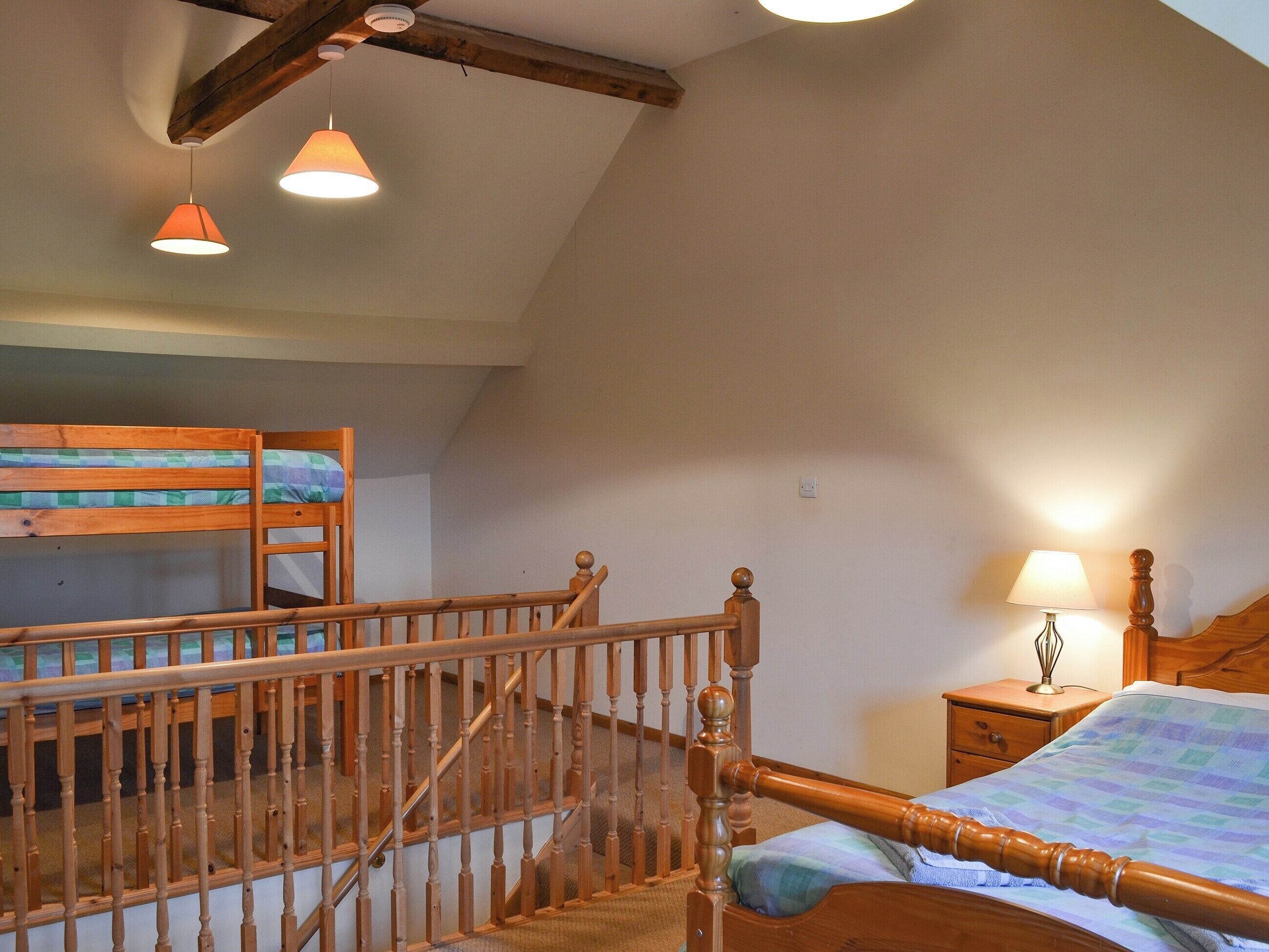 A bedroom with a wooden bunk bed, a single bed, a nightstand, a lamp, and a staircase.