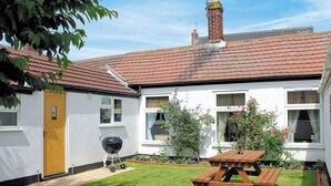 A white house with a red-tiled roof, a wooden door, and a barbecue grill in the yard. - 2 bedroom accommodation in Winterton-on-Sea, near Great Yarmouth (Winterton-on-Sea, near Great Yarmouth)