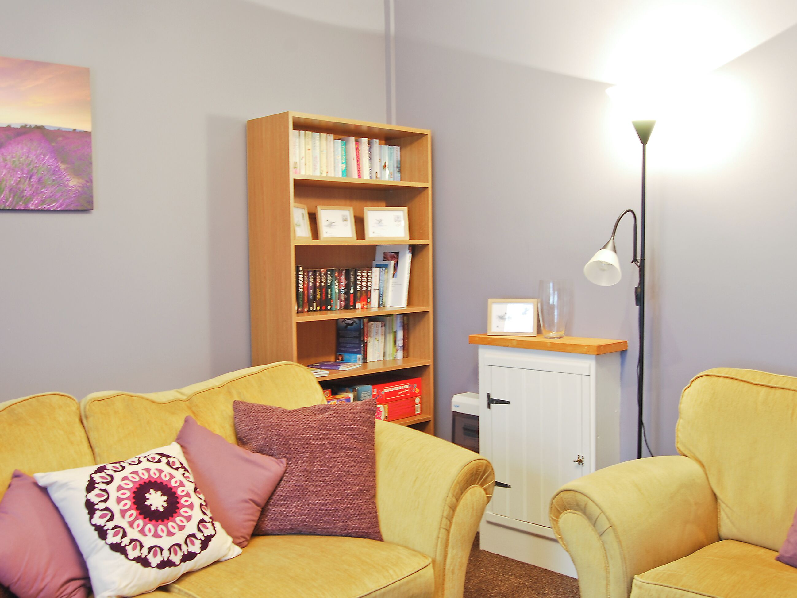 A cozy living room with a yellow sofa, a wooden bookshelf, and a white cabinet.