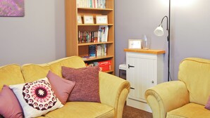 A cozy living room with a yellow sofa, a wooden bookshelf, and a white cabinet. - 2 bedroom accommodation in Winterton-on-Sea, near Great Yarmouth (Winterton-on-Sea, near Great Yarmouth)