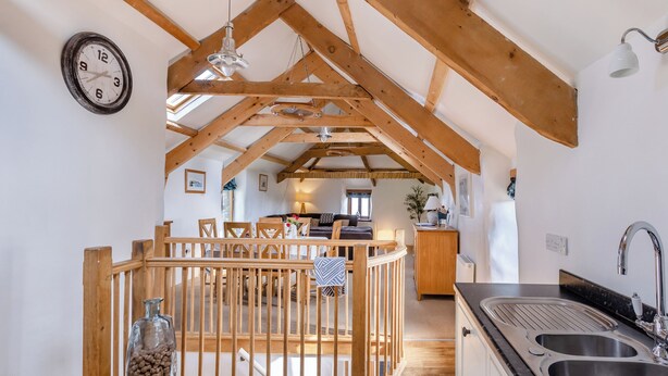 A rustic kitchen with wooden beams, a dining area with a wooden fence, and a clock on the wall.