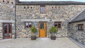 A stone building with a wooden door, two potted plants, and a gravel driveway.