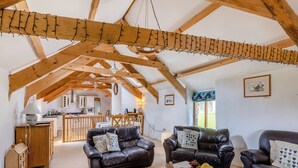 A spacious loft with exposed wooden beams, a kitchen in the background, and leather sofas.