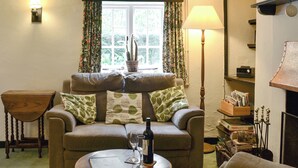 A cozy living room with a sofa, a small table, a lamp, and a window with curtains. - 3 bedroom accommodation in Passfield Common, near Liphook (Passfield Common, near Liphook)