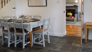A dining area with a table set for four, chairs, a clock, and a fireplace in the background.