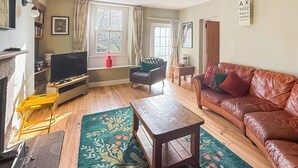 A living room with a television, leather sofa, wooden coffee table, and a patterned rug.