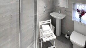A modern bathroom with a glass shower enclosure, a white sink, a toilet, and a small window with flowers.