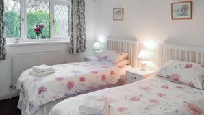 A bedroom with two beds, floral bedding, a window with curtains, a radiator, and bedside lamps.