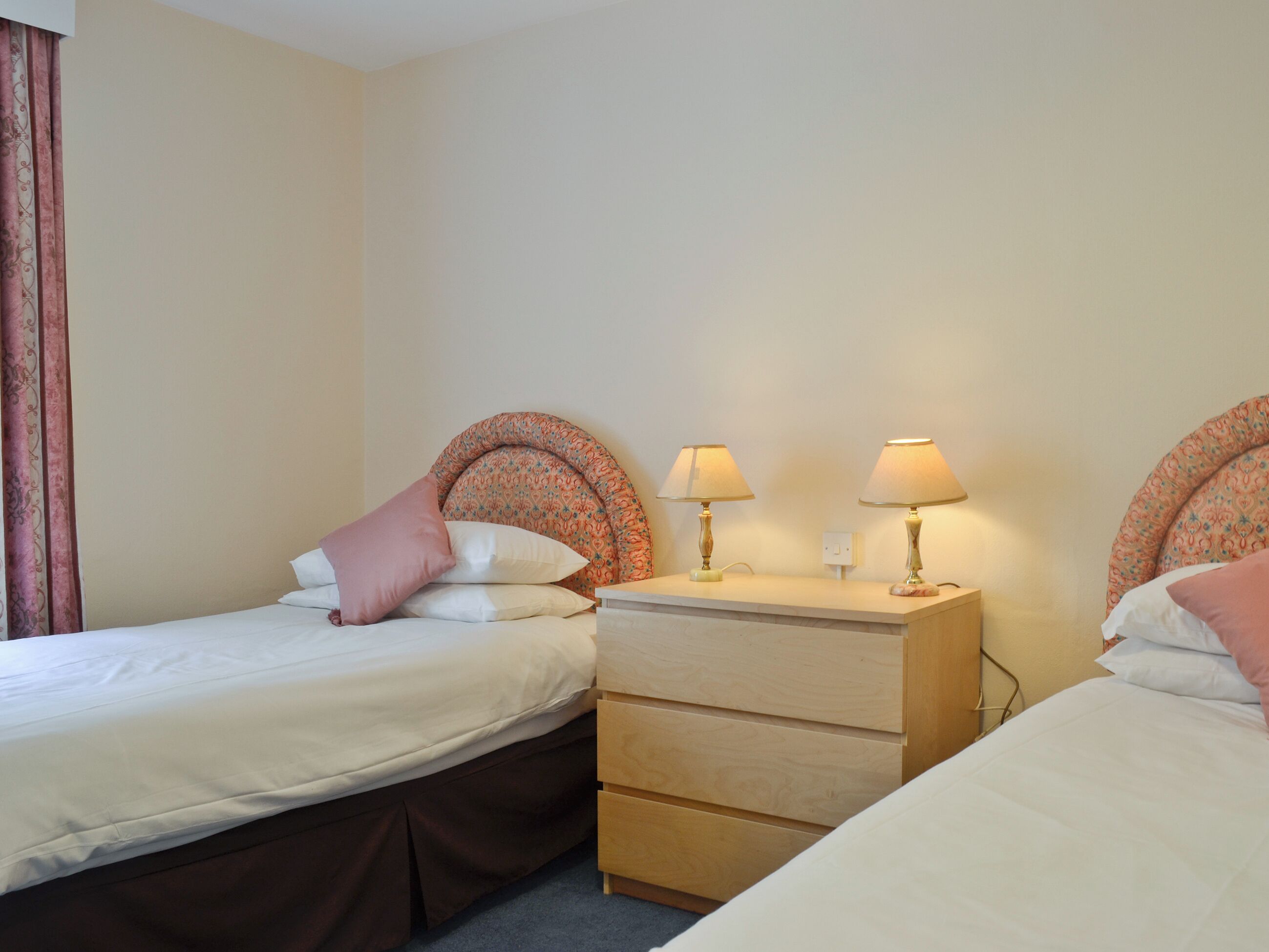 Une chambre d’hôtel avec deux lits, une table de chevet en bois et deux lampes.