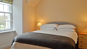 Een slaapkamer met een bed, twee nachtkastjes, een raam met gordijn, en een lamp op elk nachtkastje.