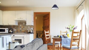 A compact kitchen with white cabinets, a microwave, and a kettle. There's a dining area with a table set for two, wooden chairs, and a checkered tablecloth.