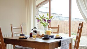 A wooden dining table with chairs, a vase with flowers, and breakfast items.