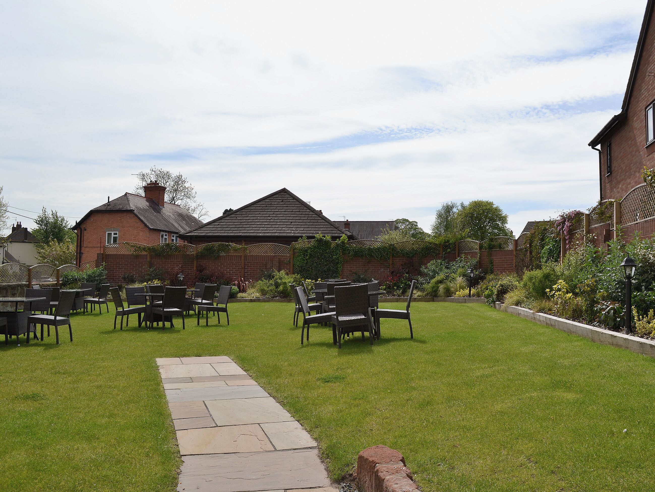 A garden with a paved walkway leading to a seating area with chairs and tables.