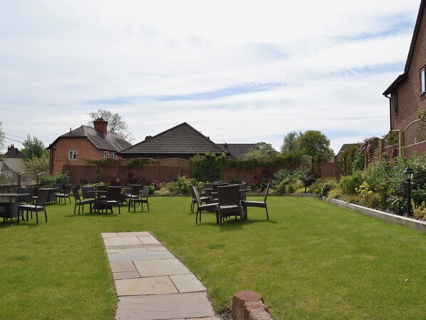 A garden with a paved walkway leading to a seating area with chairs and tables.