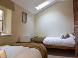 Quarto com duas camas, um radiador, janela com persianas e um claraboia.