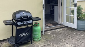 A barbecue grill with a gas cylinder and a branded bag on a patio. - Orchard Bank Cottage (Little London, near Gloucester)