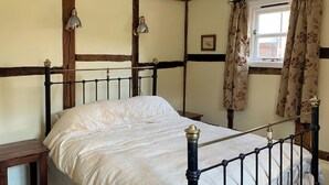 A traditional room with a four-poster bed, wooden beams, and a window with floral curtains. - Orchard Bank Cottage (Little London, near Gloucester)