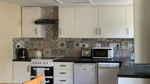 A compact kitchen with white cabinets, a toaster, a microwave, a coffee maker, and a dishwasher. - Orchard Bank Cottage (Little London, near Gloucester)