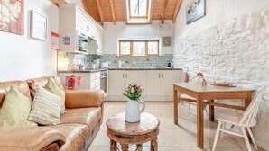 A cozy kitchen with a wooden ceiling, a stone wall, and a dining area with a table and chairs.