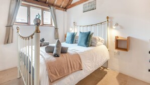 A bedroom with a wooden ceiling, a bed with a white headboard, a window with curtains, and a wall-mounted light fixture.