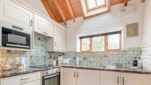 A kitchen with white cabinets, a built-in microwave, a stove, a window, and a tiled backsplash.