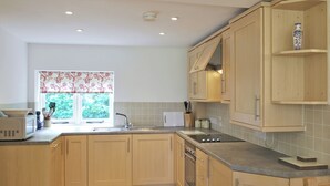 Une cuisine moderne avec des meubles en bois, un four encastré et une fenêtre agrémentée de rideaux à motifs floraux.