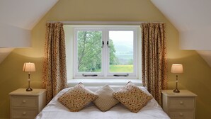 Une chambre à coucher avec un lit, deux tables de chevet avec des lampes, une fenêtre avec des rideaux et une vue sur la verdure à l’extérieur.