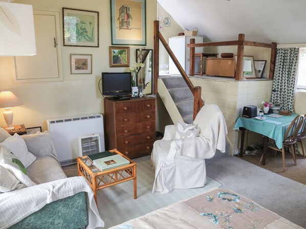 Un salon confortable avec un canapé, une petite table, un fauteuil, un escalier et un coin repas comprenant une table et des chaises.