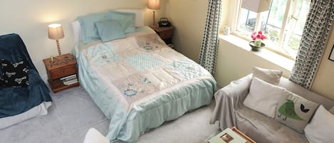 Um quarto com cama, mesas de cabeceira, uma cadeira, um sofá e uma janela com cortinas.