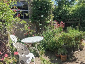 A garden with a white metal table and chair, surrounded by various plants and flowers. - 0 bedroom accommodation in Pilton, near Glastonbury (Pilton, near Glastonbury)