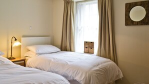 Ein Hotelzimmer mit zwei Betten, einer Nachttischlampe, einem Fenster mit Vorhängen, einem Wandspiegel und einer Deckenleuchte.