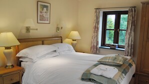 Cama bem arrumada com lençóis brancos, duas luminárias de cabeceira, um quadro na parede e uma janela com cortinas.