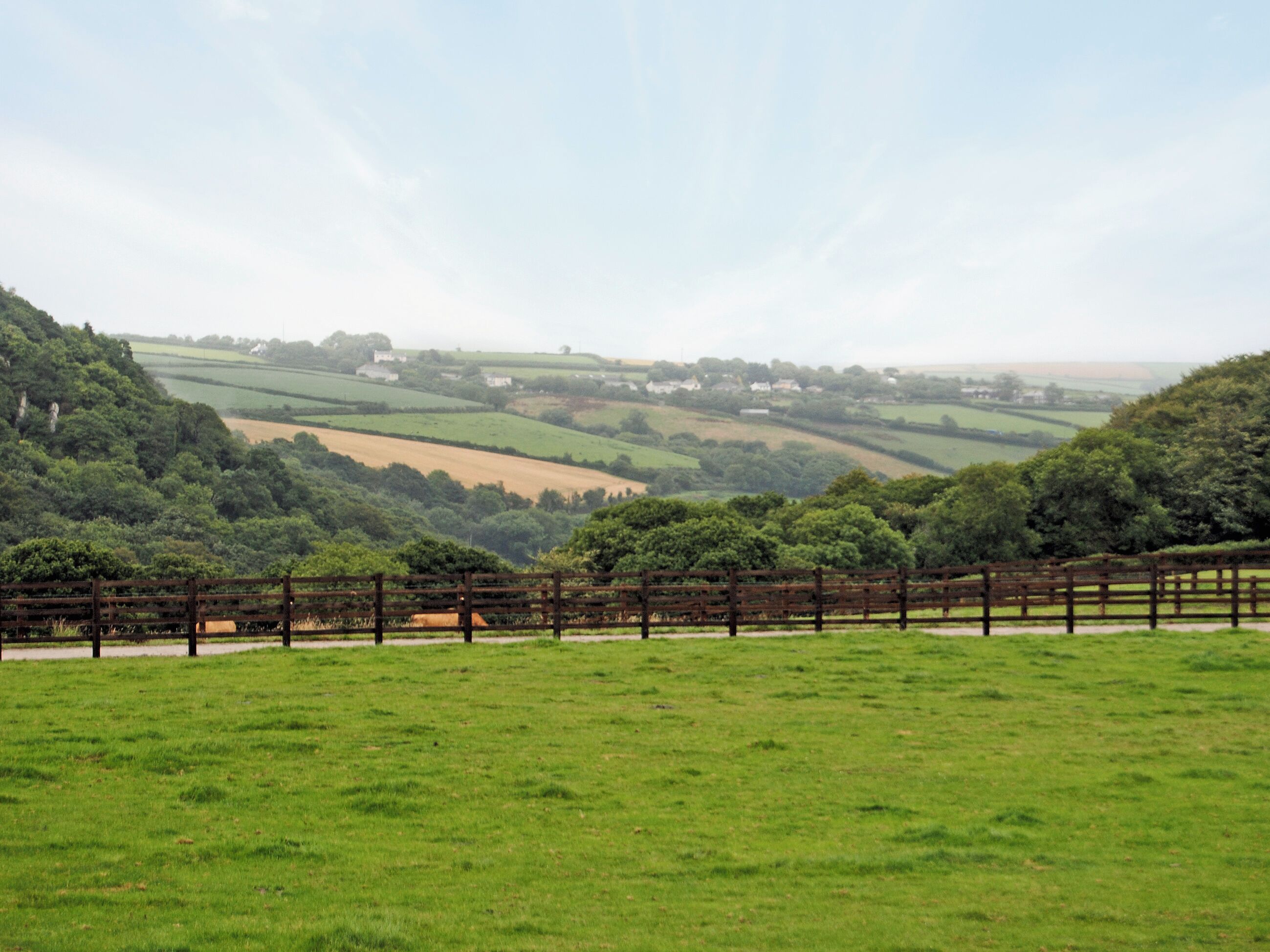 A rural landscape with rolling hills, a fenced field, and distant houses.