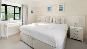 Un dormitorio ordenado con cama, mesitas de noche, un escritorio y una ventana con cortinas.