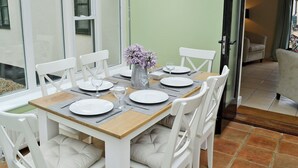 Comedor con una mesa dispuesta para cuatro, sillas blancas, un florero con flores y vista a través de un ventanal.