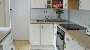 Una cocina con armarios blancos, un lavamanos de acero inoxidable, una lavadora Bosch y un horno empotrado.